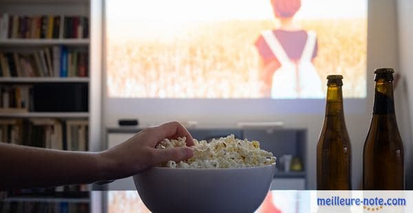 main qui attrape du popcorn en regardant un film sur un vidéoprojecteur