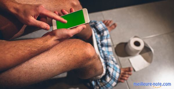 Un homme qui joue avec son smartphone sur un wc portable