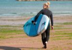 jeune femme qui transporte son paddle sur la plage